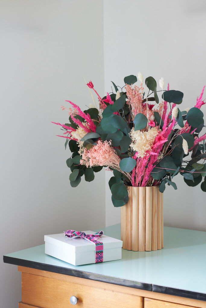 Vase en tuyau de plomberie avec un revêtement en demi-rond de bois avec un bouquet et un cadeau posé à côté